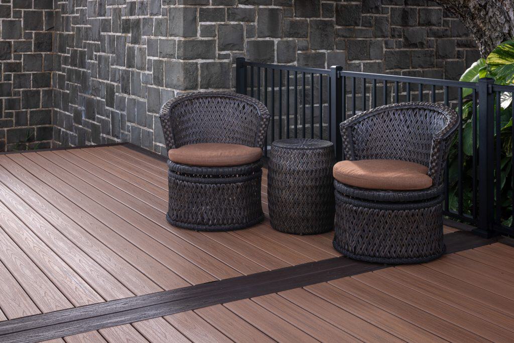 Trex Transcend deck boards in Tiki Torch and Lava Rock with a double transition border, showcasing a seamless design. The photo includes outdoor furniture, featuring two round wicker chairs that complement the space, as well as the Trex Black Signature railing system. This stylish and modern outdoor space highlights quality craftsmanship and a cohesive aesthetic in Honolulu.