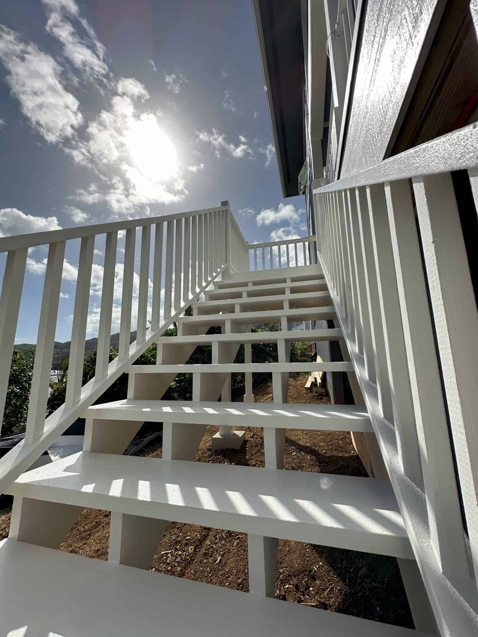 Custom build wood stairs painted white looking up towards the Hawaiian blue sky and the sun to emphasize the bright and clean construction.