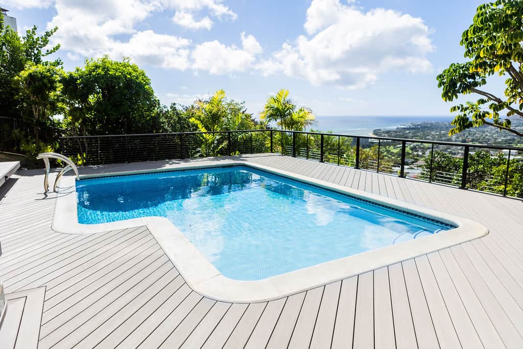 Full pool deck photo of the deck with Azek TimberTech PVC deck boards and Feeney stainless steel cable railing, capturing the ocean and greenery surrounding the Honolulu home.