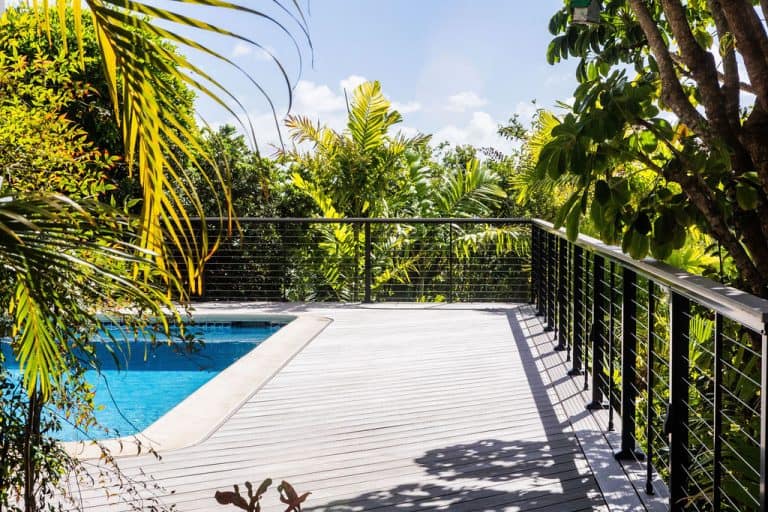 Side profile of a modern deck featuring Azek TimberTech PVC deck boards in Vintage Coastline with a diagonal pattern. On the left, the pool is visible, and lush greenery surrounds the deck.