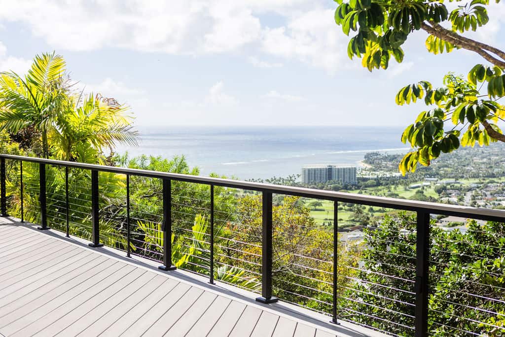 Modern deck featuring Azek TimberTech advanced PVC deck boards in Vintage Coastline, with a double border and diagonal design. Feeney stainless steel cable railing with black aluminum posts and a TimberTech drink rail complement the beautiful Honolulu home with an ocean view.