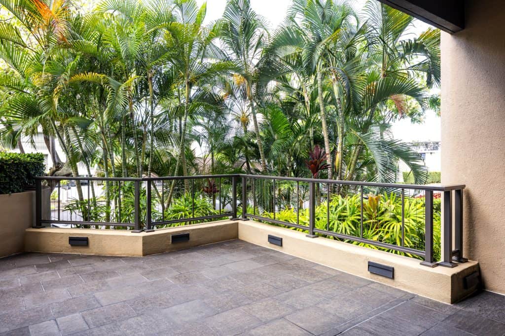 Black Feeney vertical cable railing with stainless steel cables installed for an AOAO in Honolulu, set against a lush tropical backdrop with palm trees and greenery.
