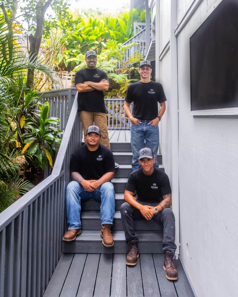 The Hilweh Builders and Hawaii Deck Builders team—Chad, Tama, Noah, and Tiger—standing together, wearing black branded shirts and hats, looking at the camera with tropical greenery behind them.