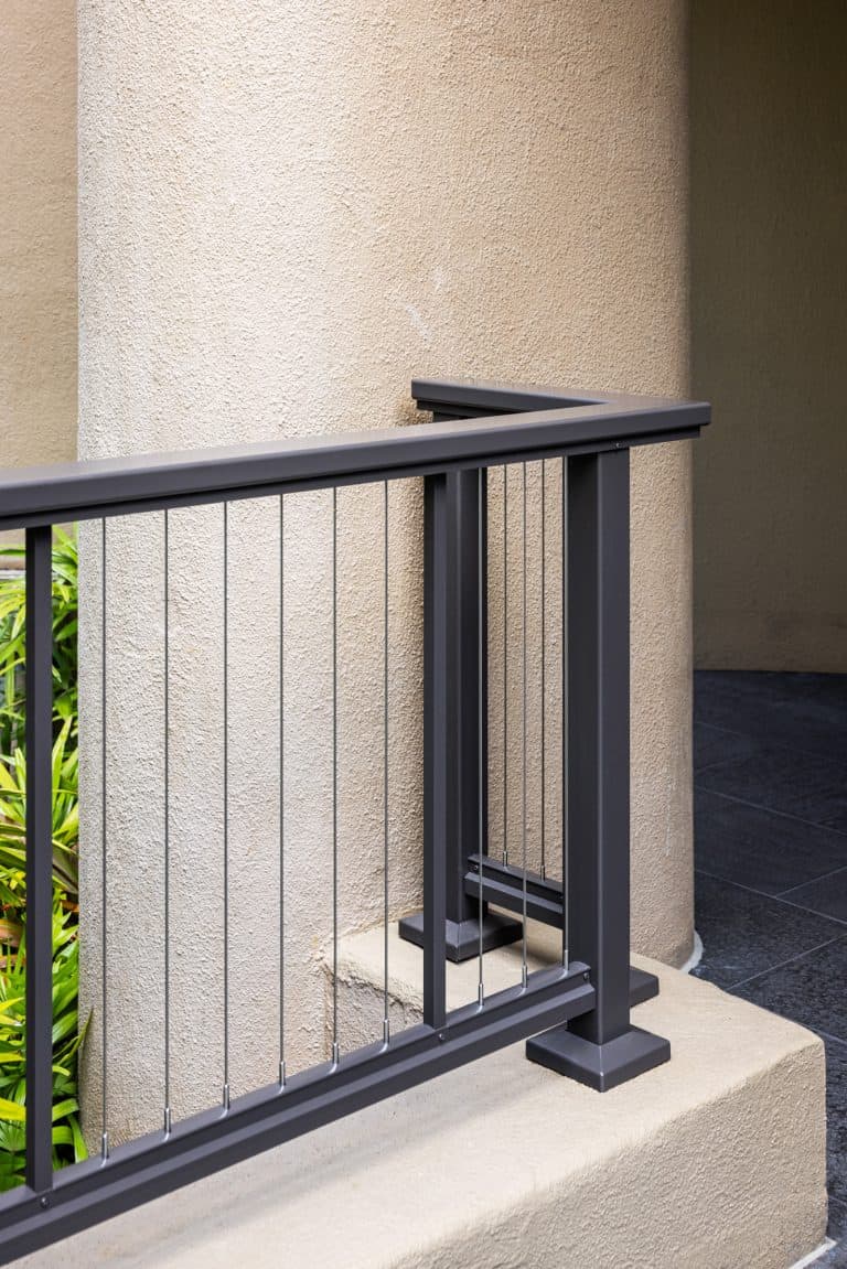 Detail view of a black Feeney cable railing system wrapping around a round column at a Honolulu condominium, with subtle tropical greenery in the background.