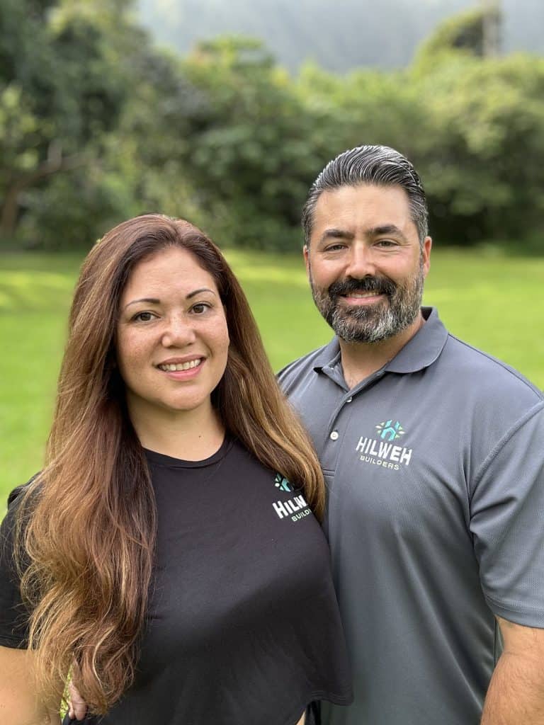 Chad and Liana Hilweh, owners of Hawaiʻi Deck Builders, wearing branded shirts with a scenic green nature background