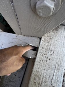 Finger poking through wood deck board that is painted showing that the wood under the paint has failed and this deck is no longer safe.